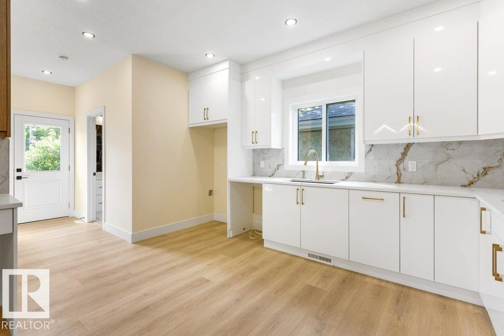 Bright, open kitchen featuring white cabinetry with brushed gold hardware, marble-look backsplash, and stainless steel appliances - 10323 79 Street Nw, Edmonton, AB - Indoor Photo Showing Kitchen