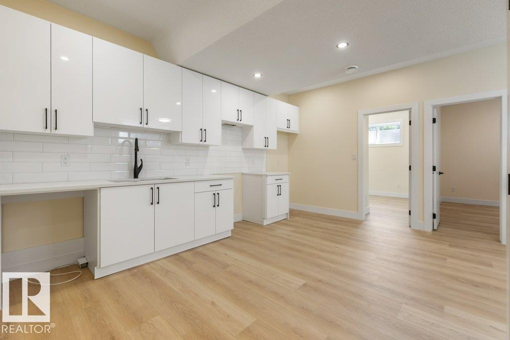 Modern kitchen featuring white high-gloss cabinetry, matte black hardware, white subway tile backsplash, and light wood-finish flooring - 10323 79 Street Nw, Edmonton, AB - Indoor Photo Showing Kitchen