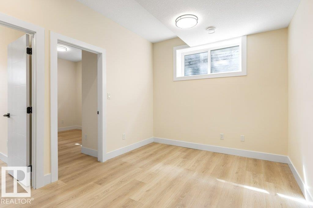 Versatile interior space featuring wood-finish flooring, light-toned walls, and bright overhead lighting - 10323 79 Street Nw, Edmonton, AB - Indoor Photo Showing Other Room