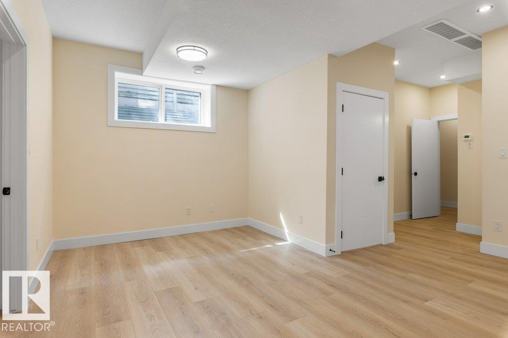 Spacious room featuring wood-finish flooring, light-toned walls, and white baseboards - 10323 79 Street Nw, Edmonton, AB - Indoor Photo Showing Other Room