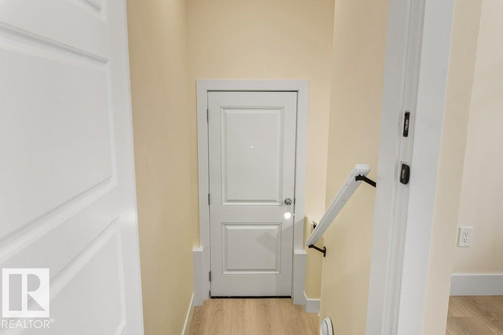 Secondary Suite Entrance - Hallway featuring a white paneled door, light wood-finish flooring, light beige wall paint, white baseboards, and a white handrail with dark brackets - 10323 79 Street Nw, Edmonton, AB - Indoor Photo Showing Other Room