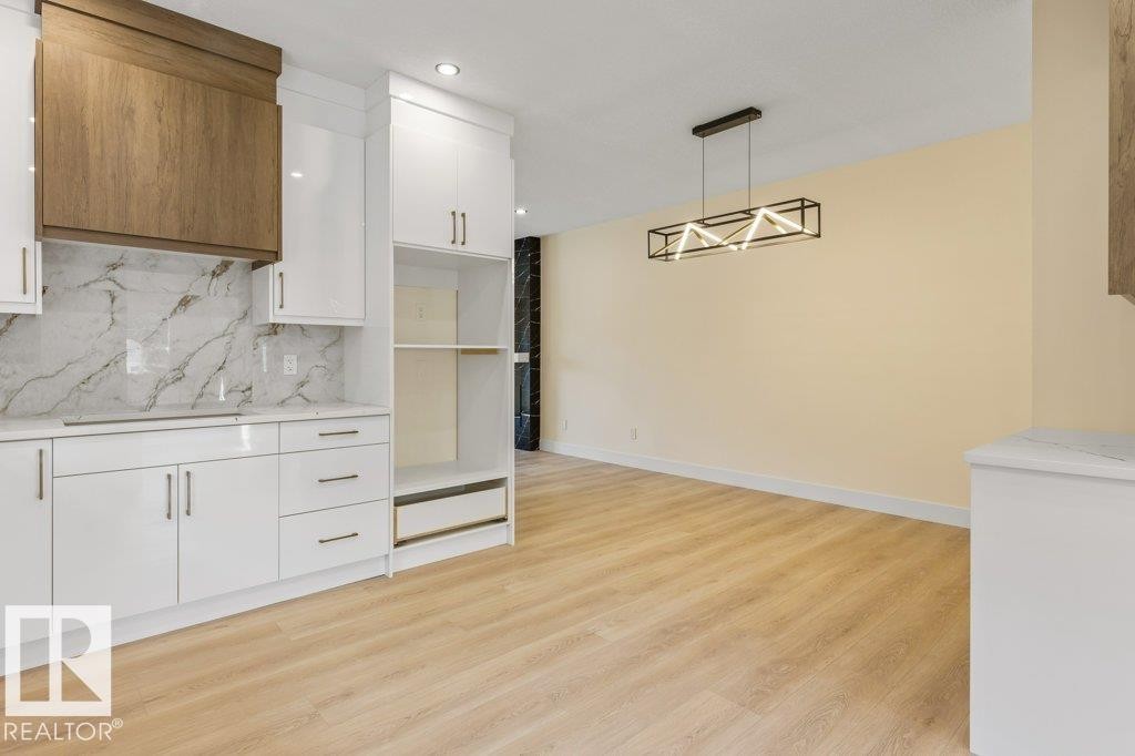 Modern open-concept living space featuring white cabinetry with marble backsplash, wood-finish flooring throughout, stainless steel appliances, and abundant natural lighting from recessed ceiling fixtures - 10323 79 Street Nw, Edmonton, AB - Indoor Photo Showing Kitchen