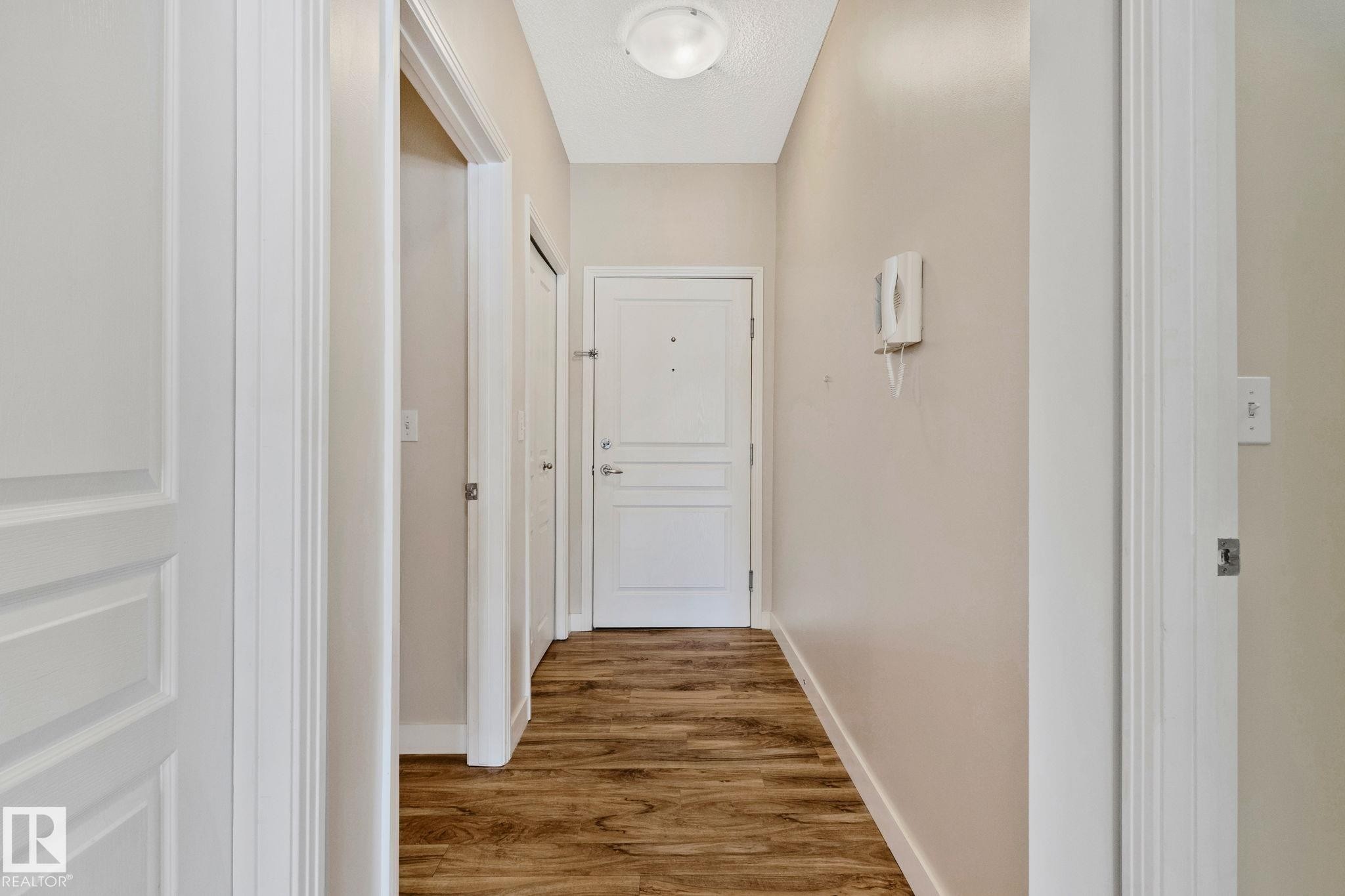 Bright hallway featuring warm wood-finish flooring, clean white trim work, and multiple white panel doors with polished hardware - #120 8931 156 St Nw, Edmonton, AB