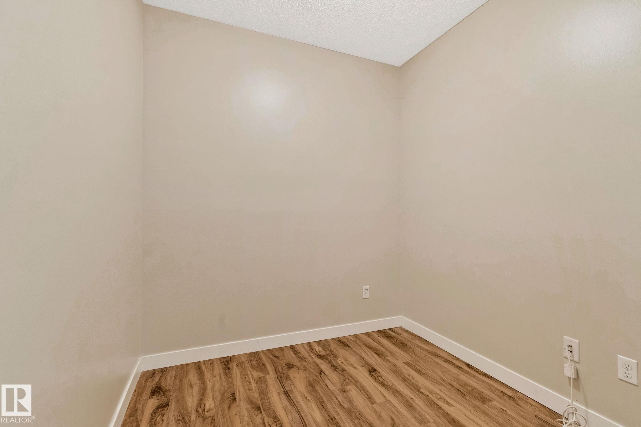 Room featuring wood-finish flooring, light-toned walls, and white baseboards - #120 8931 156 St Nw, Edmonton, AB