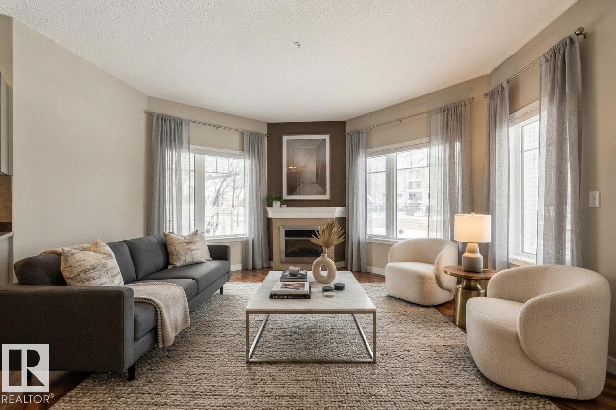Living area featuring wood-finish flooring, a built-in fireplace, and expansive windows - #120 8931 156 St Nw, Edmonton, AB