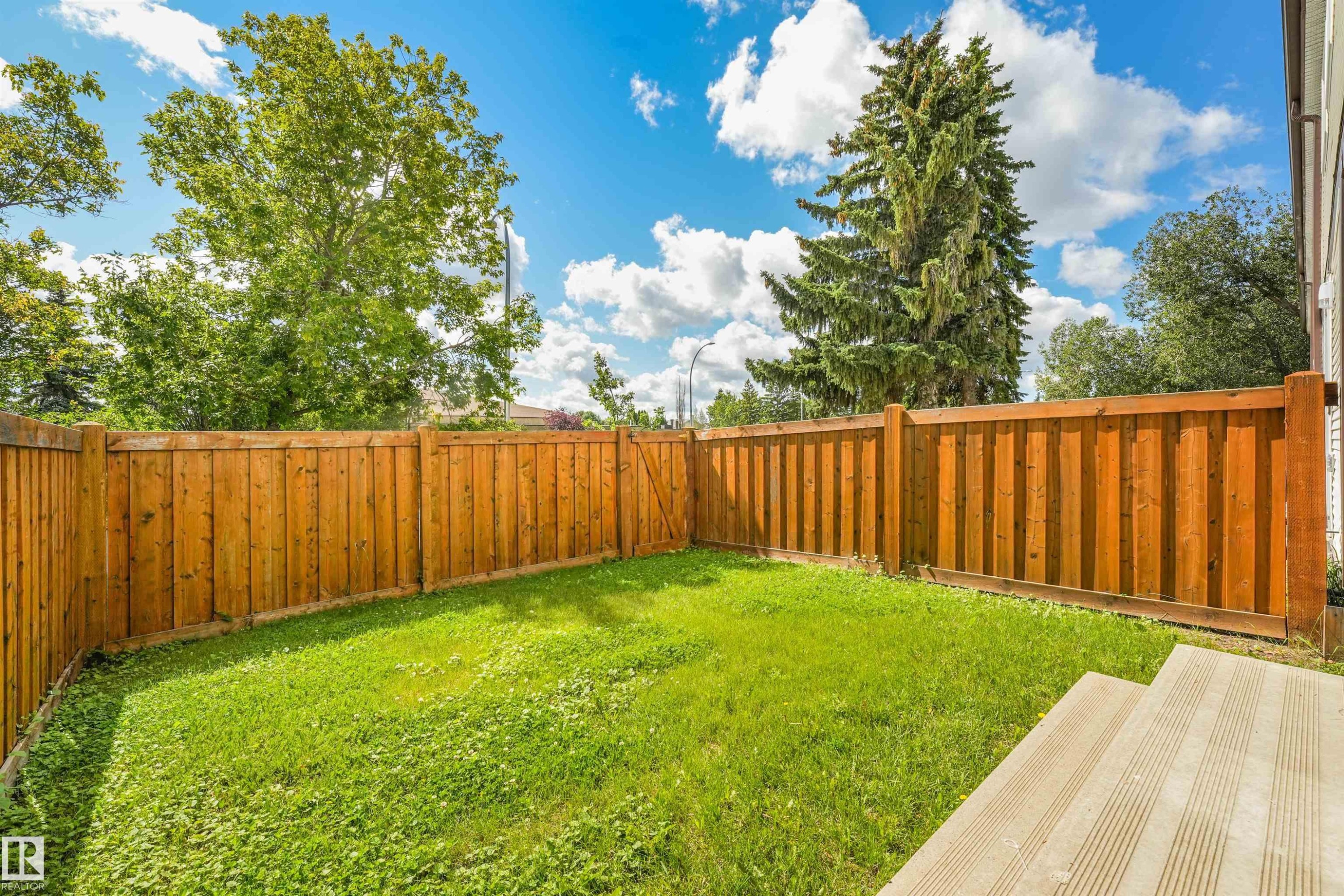 Expansive rear yard featuring green lawn, full privacy fencing, and wood-toned decking - #39 14511 52 Street Nw, Edmonton, AB - Outdoor