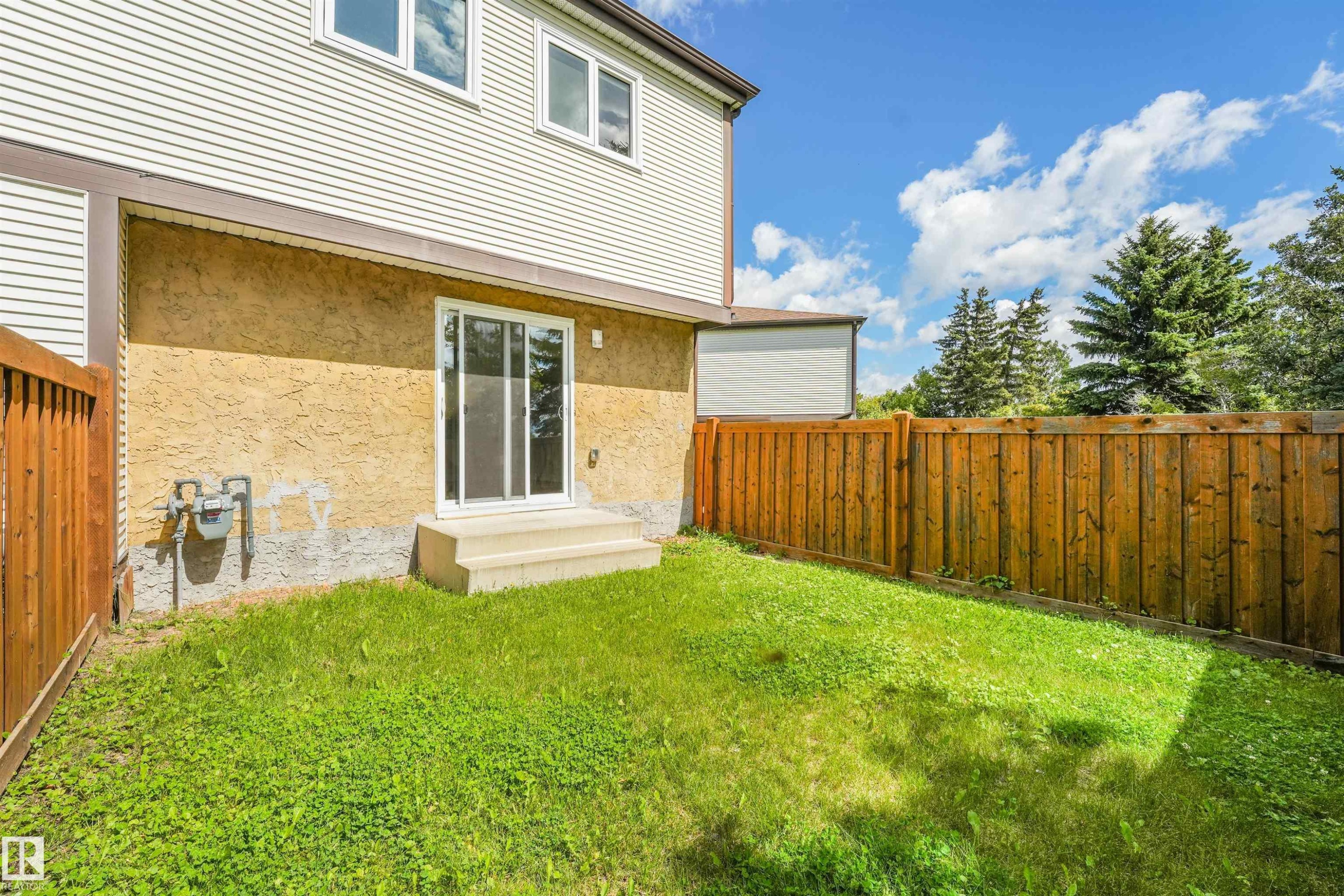 Expansive backyard featuring a sliding glass door, concrete steps, wood fencing, and a manicured lawn - #39 14511 52 Street Nw, Edmonton, AB - Outdoor