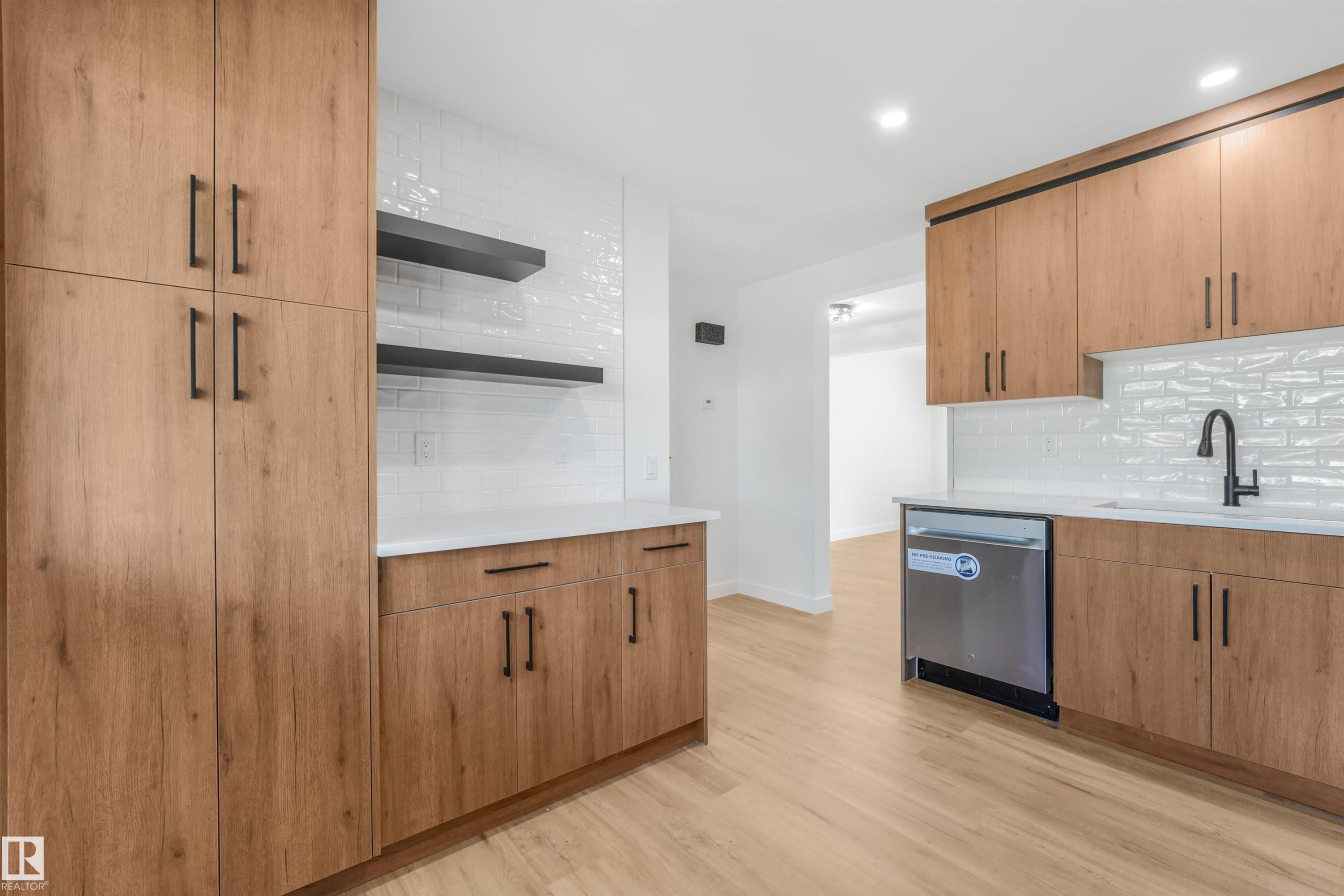 Kitchen featuring extensive wood-finish cabinetry, white subway tile backsplash, stainless steel dishwasher, matte black faucet, and light wood-finish flooring - #39 14511 52 Street Nw, Edmonton, AB - Indoor Photo Showing Kitchen