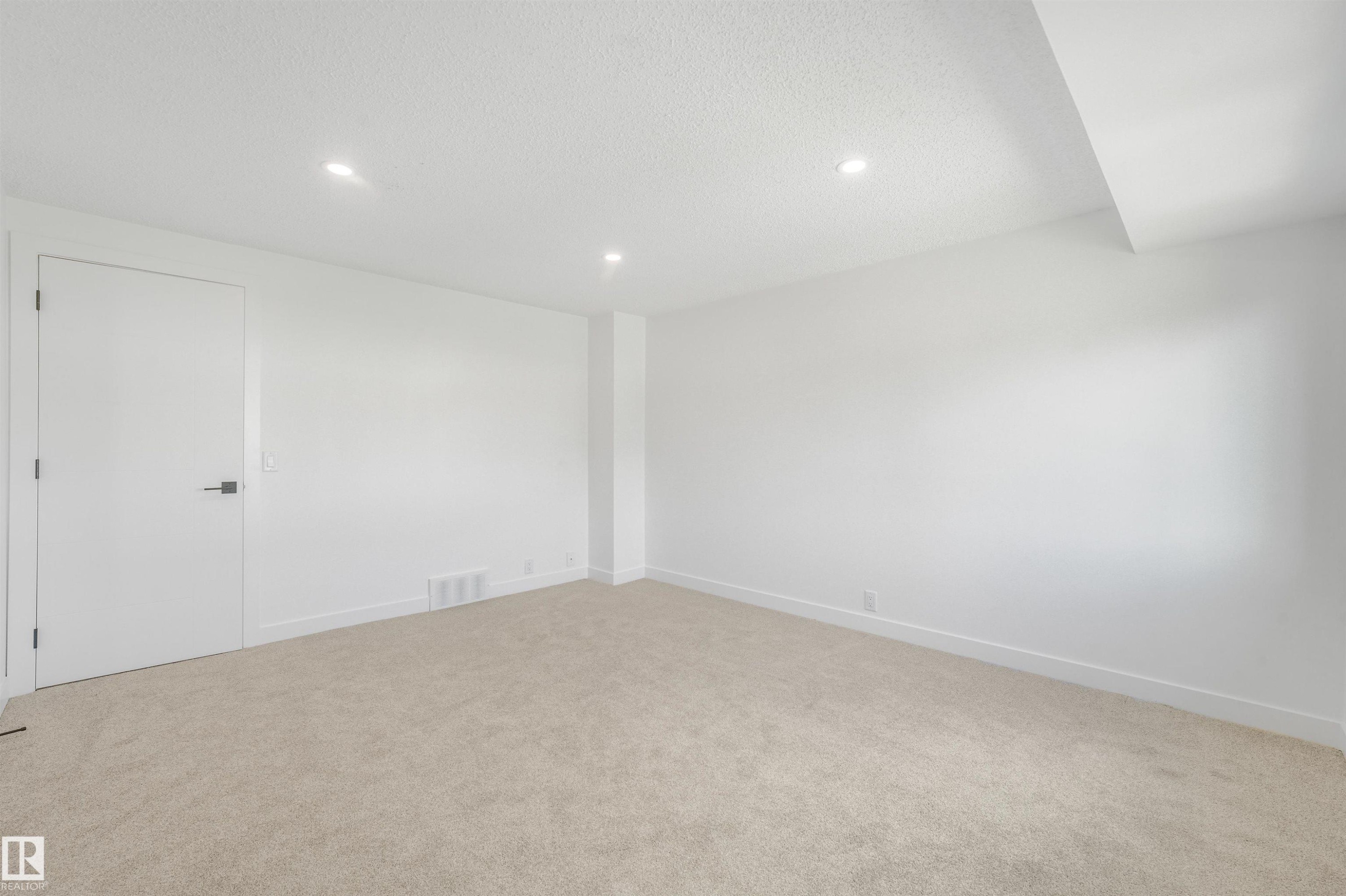 Spacious room featuring neutral carpeting, white walls, recessed lighting, and a modern interior door with black hardware - #39 14511 52 Street Nw, Edmonton, AB - Indoor Photo Showing Other Room