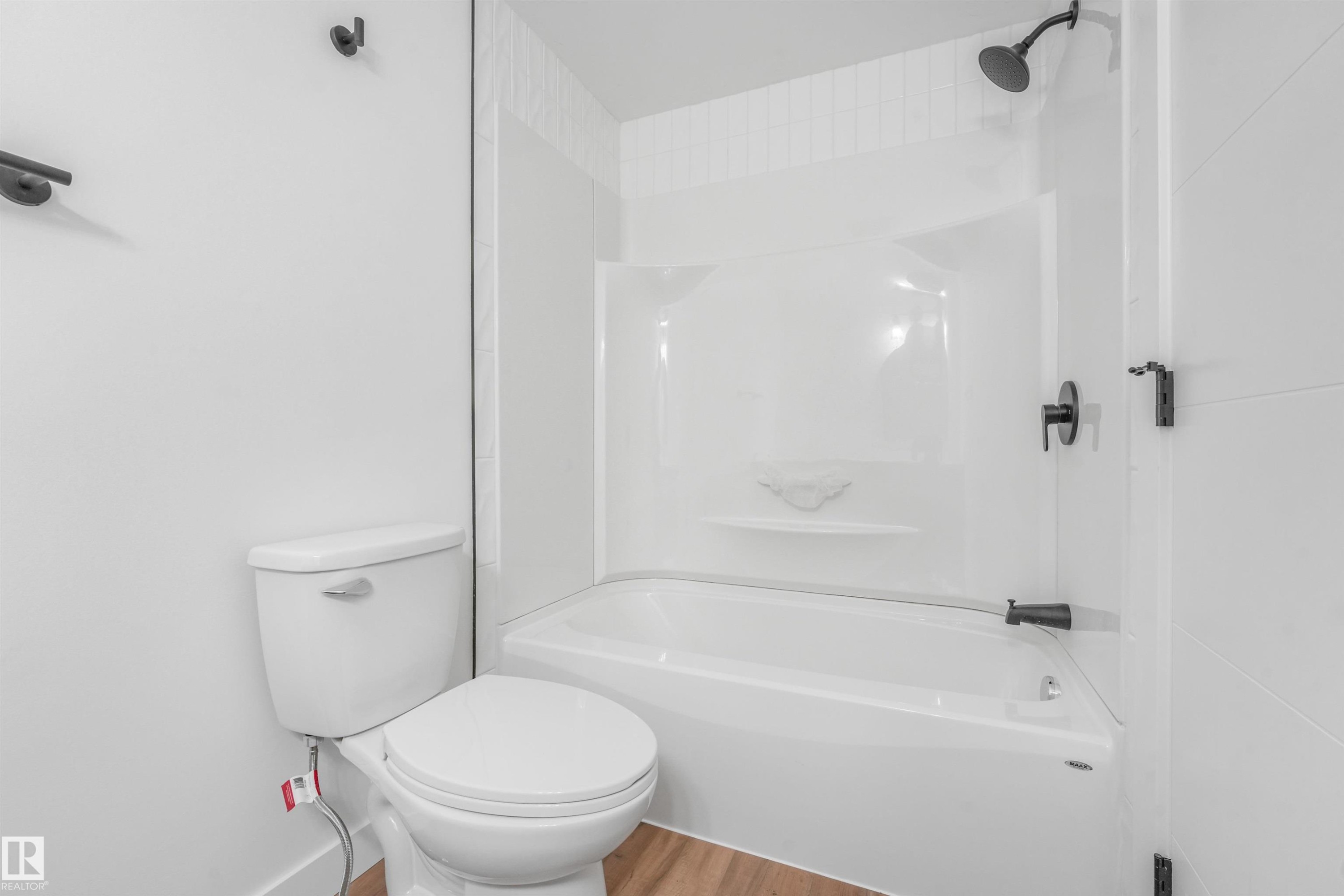 Bathroom featuring a white bathtub and shower combination with dark-finished fixtures, a white toilet, and wood-finish flooring - #39 14511 52 Street Nw, Edmonton, AB - Indoor Photo Showing Bathroom