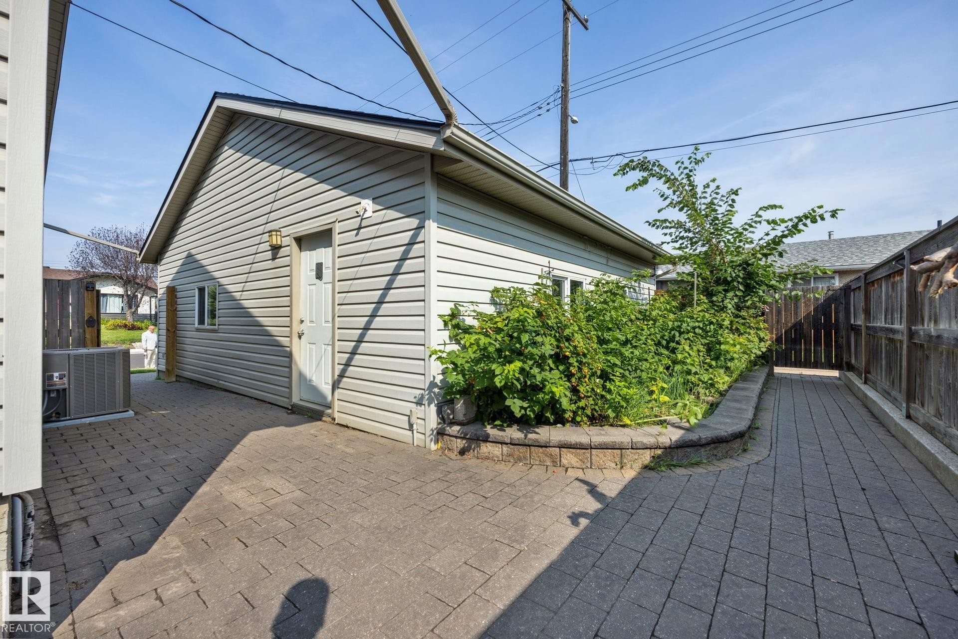 Spacious paved patio with permeable pavers extending across the backyard, complemented by mature landscaping and vinyl-sided cottage structure with peaked roofline - 9503 54 Street Nw, Edmonton, AB