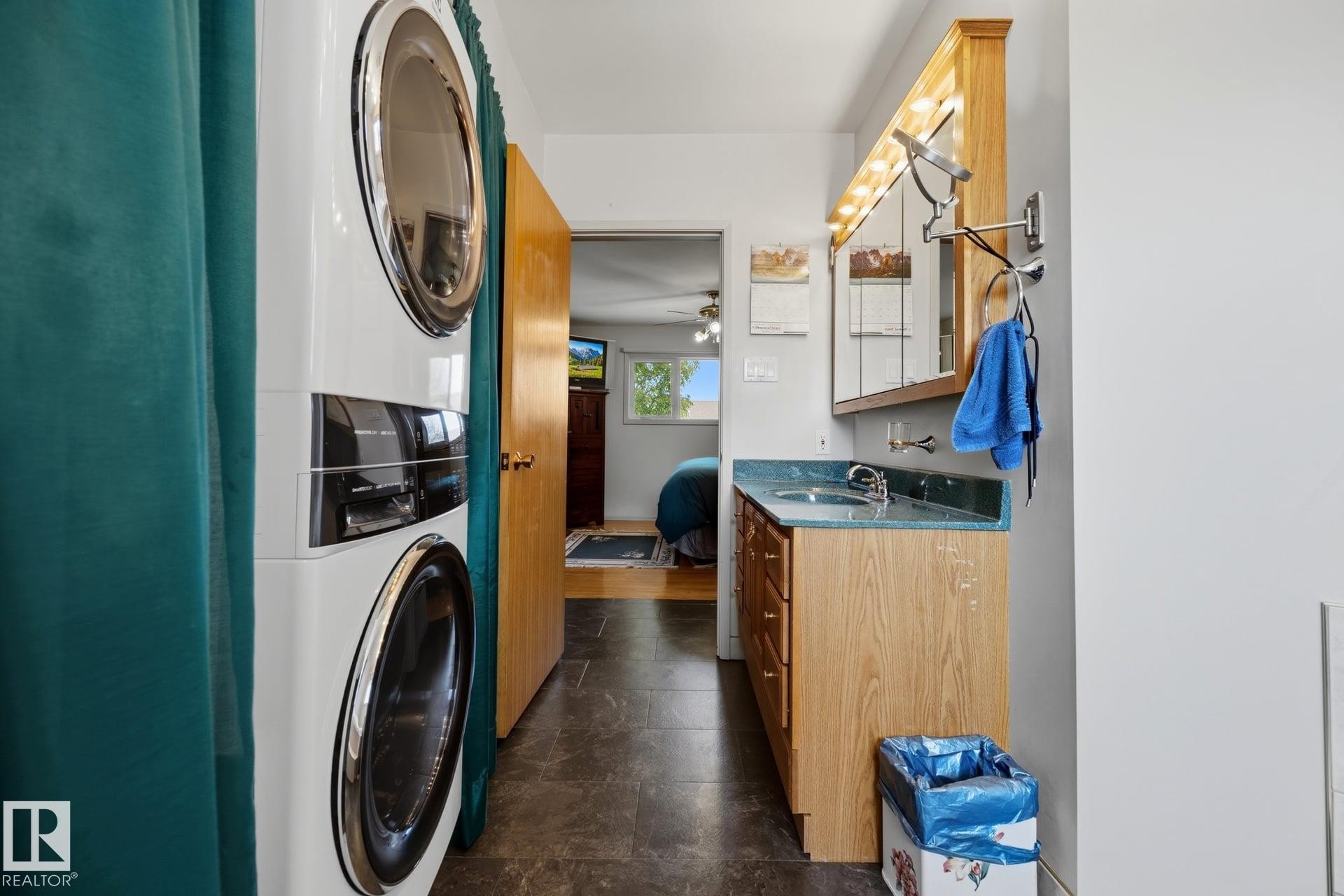 Stacked laundry appliances, wood-finish vanity with countertop, integrated sink, and mirrored medicine cabinet - 9503 54 Street Nw, Edmonton, AB