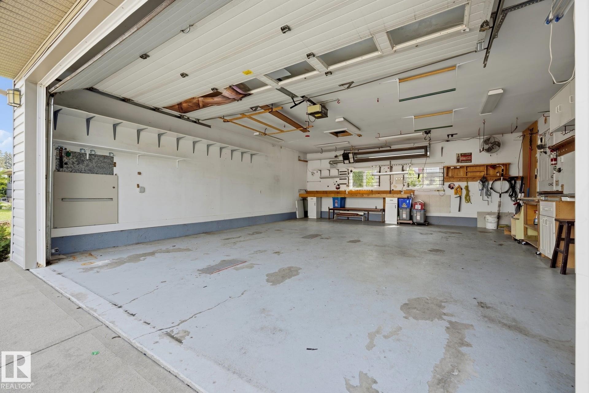 Spacious two-car garage with epoxy-coated concrete flooring, wall-mounted storage systems, built-in cabinetry, and overhead lighting throughout - 9503 54 Street Nw, Edmonton, AB