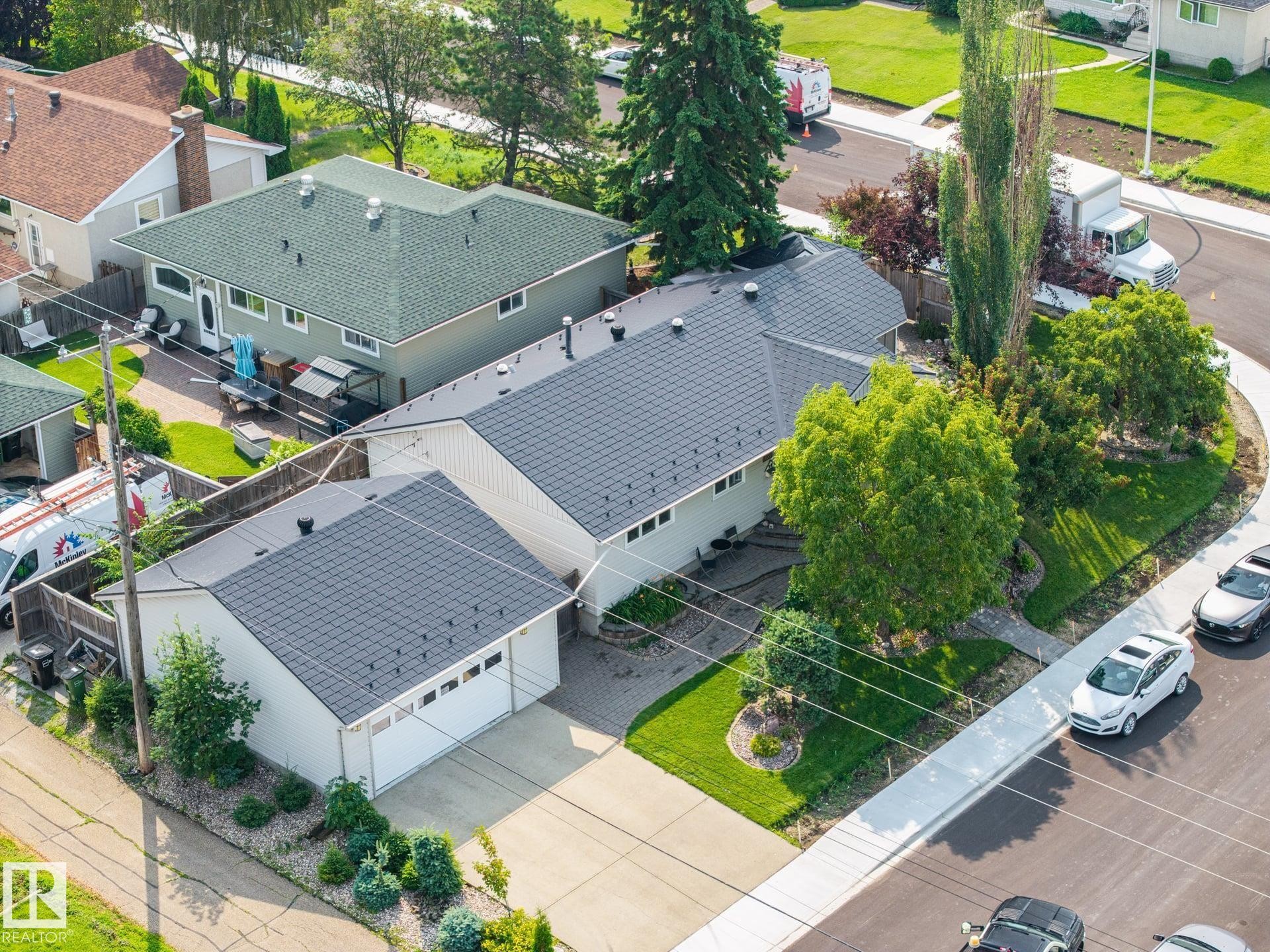 Paved driveway leading to an attached garage, landscaped front yard with mature trees, and a gray shingle roof - 9503 54 Street Nw, Edmonton, AB