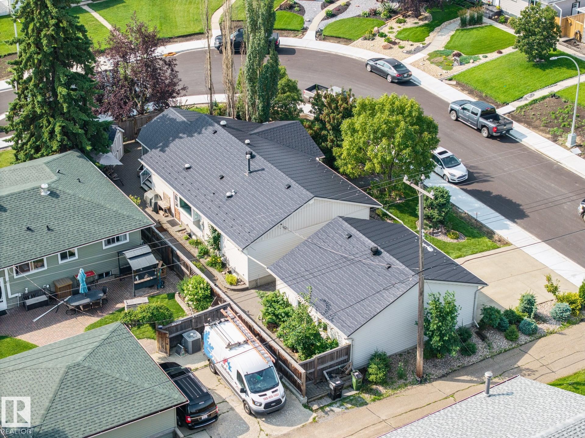 Modern residence featuring a dark charcoal composite roof, clean white exterior siding, and mature landscaping with tall columnar trees - 9503 54 Street Nw, Edmonton, AB