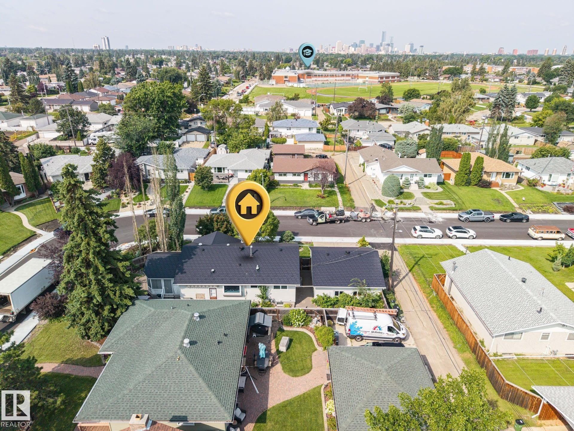 Aerial view showcasing this residential property featuring a dark-shingle roof, manicured lawn with mature landscaping, brick and stone exterior finishes, and a driveway with parking - 9503 54 Street Nw, Edmonton, AB