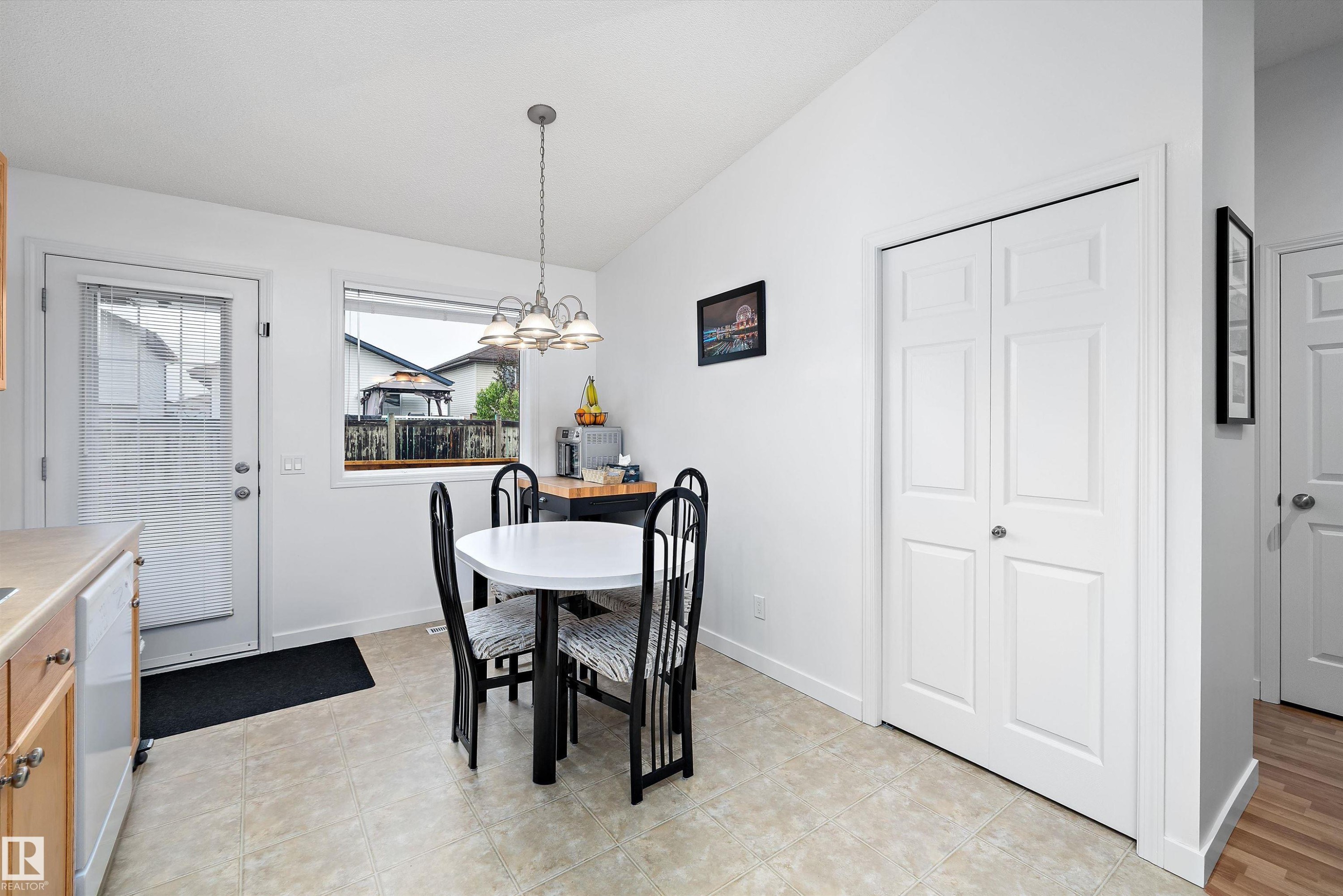 Kitchen dining area featuring neutral tile flooring, a window, a single exterior door, light wood-finish cabinetry, and a bi-fold closet - 3344 24 Avenue Nw, Edmonton, AB - Indoor Photo Showing Dining Room
