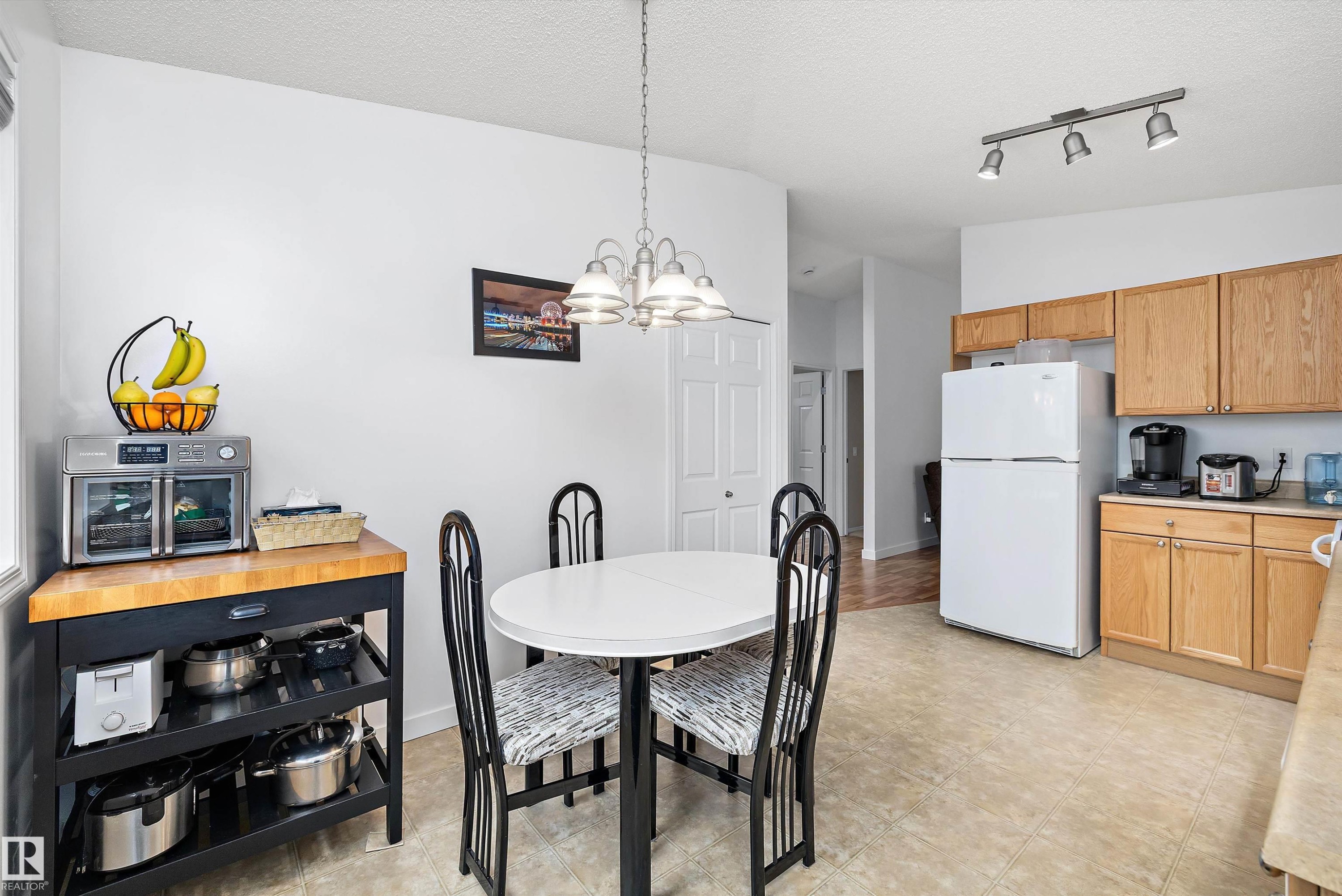 Kitchen and dining area featuring light wood-finish cabinetry, a white refrigerator, and a track light fixture - 3344 24 Avenue Nw, Edmonton, AB - Indoor