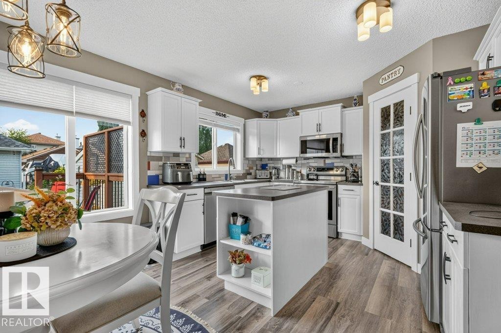 Kitchen featuring white cabinetry with dark hardware, a center island with open shelving, wood-finish flooring, and integrated stainless steel appliances - 5322 Terwillegar Boulevard Nw, Edmonton, AB - Indoor