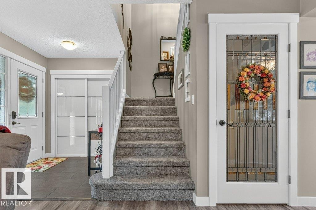 Carpeted staircase with white railing, wood-finish flooring, and a white door with decorative glass panels - 5322 Terwillegar Boulevard Nw, Edmonton, AB - Indoor Photo Showing Other Room