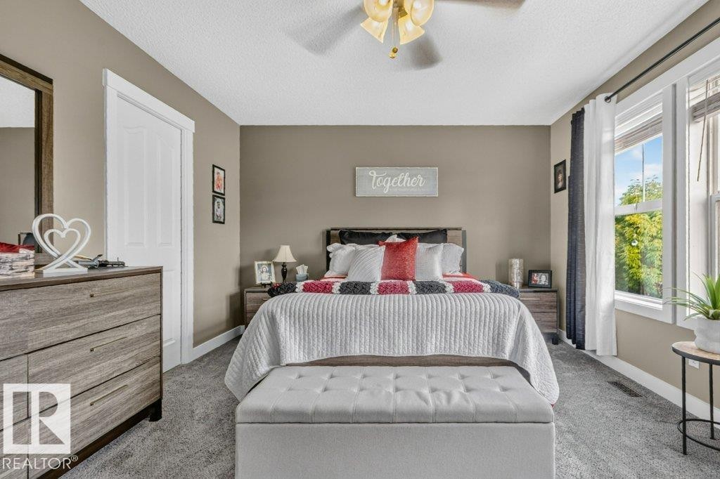 Wall-to-wall carpeting, multiple windows providing natural light, a ceiling fan with integrated lighting, and a white paneled door with matching trim - 5322 Terwillegar Boulevard Nw, Edmonton, AB - Indoor Photo Showing Bedroom