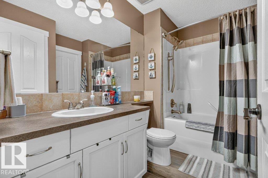 Bathroom featuring a white vanity with panel cabinetry and brushed nickel hardware, a dark countertop, a large mirror, a tile backsplash, and a tub/shower combination with a tile surround - 5322 Terwillegar Boulevard Nw, Edmonton, AB - Indoor Photo Showing Bathroom