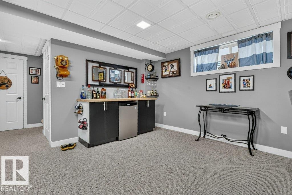 Basement recreation space featuring a built-in wet bar with a light wood-finish countertop, dark cabinetry, and a stainless steel undercounter refrigerator - 5322 Terwillegar Boulevard Nw, Edmonton, AB - Indoor Photo Showing Other Room