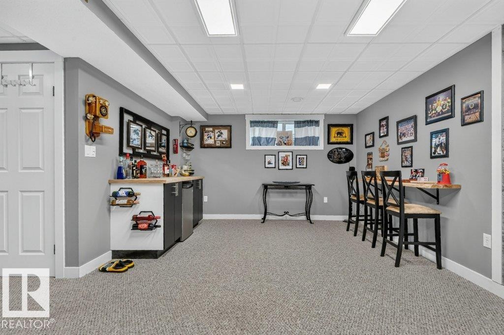 Finished lower level featuring a built-in wet bar with dual beverage refrigerators, drop ceiling with recessed lighting, wall-mounted bar table with stools, and neutral-toned carpeting throughout - 5322 Terwillegar Boulevard Nw, Edmonton, AB - Indoor