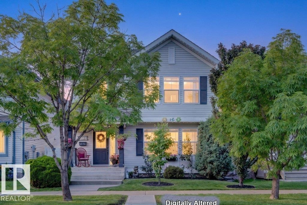 Traditional two-story home featuring light-colored siding, dark window shutters, a prominent front gable, a welcoming front porch, and mature trees in the front yard - 5322 Terwillegar Boulevard Nw, Edmonton, AB - Outdoor
