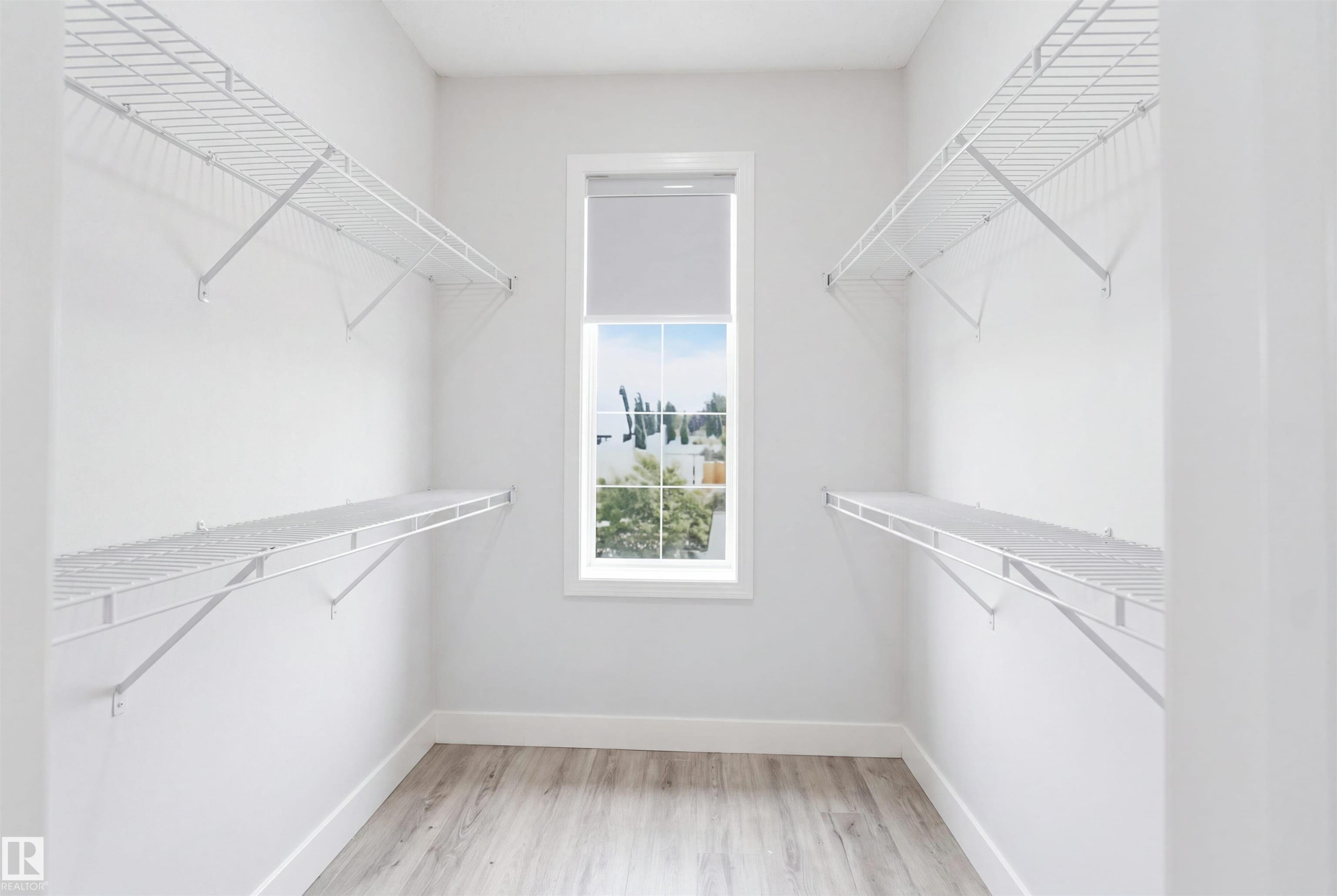 Walk-in closet featuring light wood-finish flooring, white wire shelving, a window with a roller shade, and white baseboards - 714 87 Street Sw, Edmonton, AB - Indoor With Storage