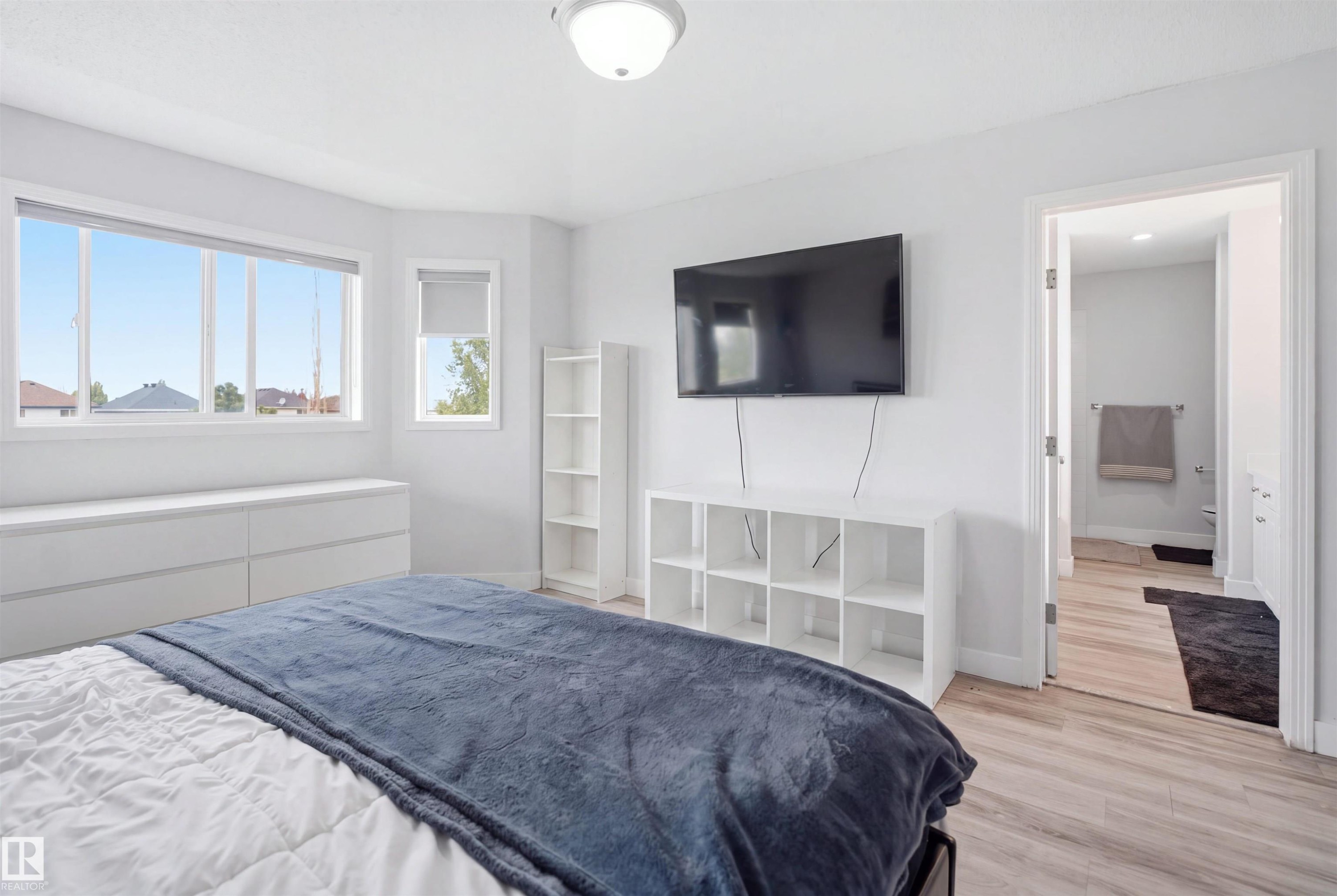 Bright bedroom featuring a large multi-pane window, an additional window with a roller shade, and wood-finish flooring - 714 87 Street Sw, Edmonton, AB - Indoor Photo Showing Bedroom