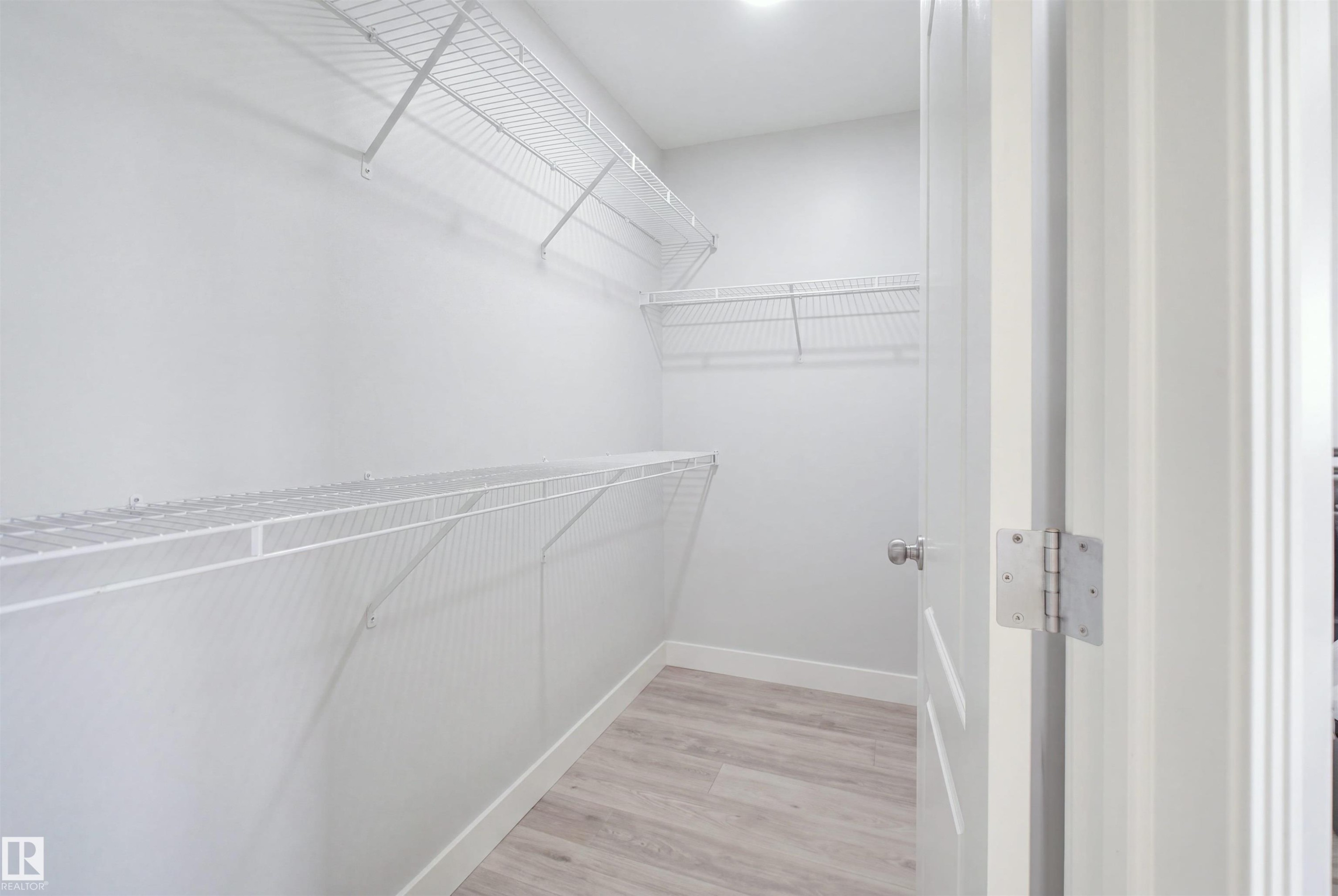 Walk-in closet featuring light wood-finish flooring, white wire shelving, and a bright overhead light fixture - 714 87 Street Sw, Edmonton, AB - Indoor With Storage