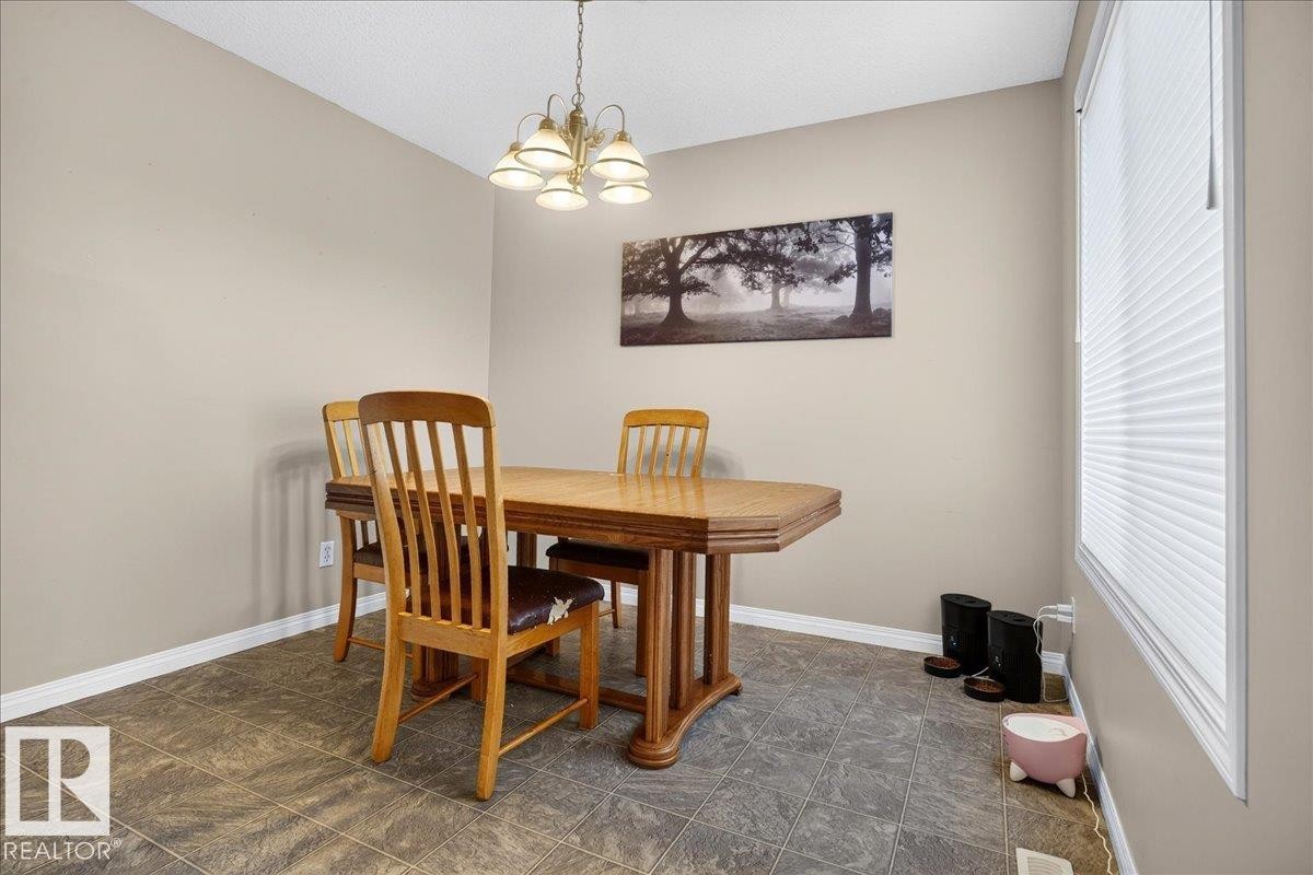 Dedicated dining room featuring a wood-finish table with pedestal base, vertical slat-back chairs, tile flooring, and a pendant light fixture - 887 Oakland Boulevard, Devon, AB - Indoor Photo Showing Dining Room