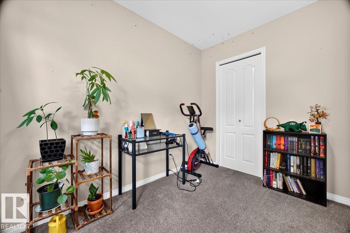 Versatile home office featuring carpet flooring, a black metal desk with ample work surface, built-in black shelving with storage capacity, a white six-panel closet door, and abundant natural light from recessed ceiling fixtures - 887 Oakland Boulevard, Devon, AB - Indoor