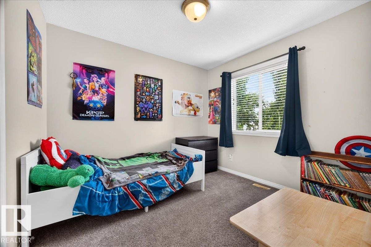 Bright secondary bedroom featuring carpeted flooring, large windows with blackout curtains, white bed frame, wood-finish desk, and colorful wall art - 887 Oakland Boulevard, Devon, AB - Indoor Photo Showing Bedroom