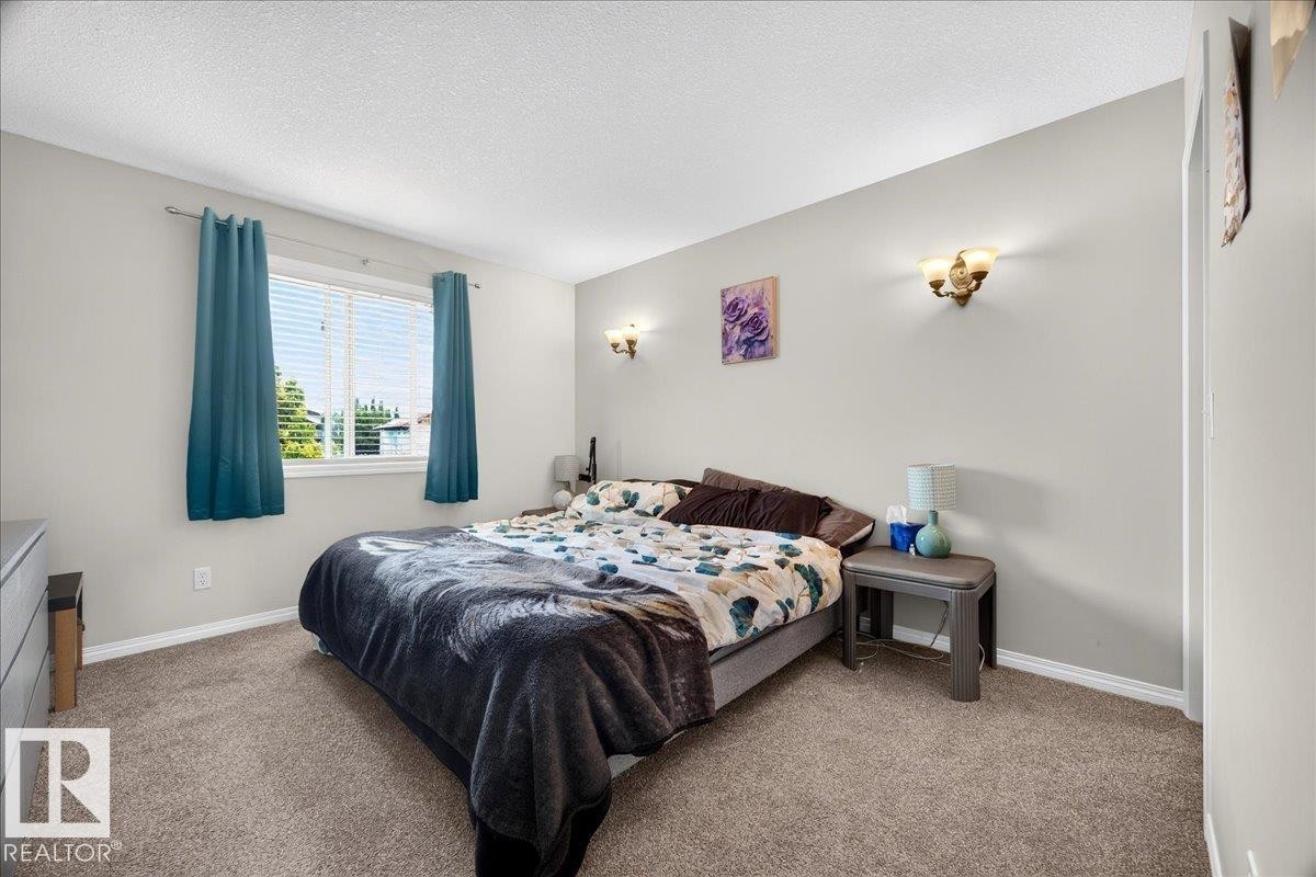 Spacious primary bedroom featuring neutral wall finishes, carpeted flooring, dual nightstands with integrated lighting, and large windows with thermal-lined drapery - 887 Oakland Boulevard, Devon, AB - Indoor Photo Showing Bedroom