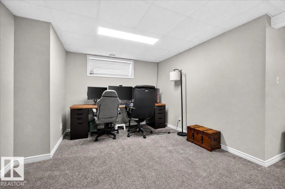 Dedicated home office featuring dual wood-finish desks with ample workspace, comfortable ergonomic seating, recessed ceiling lighting, carpeted flooring, and a high-set window with blinds for natural light and privacy - 887 Oakland Boulevard, Devon, AB - Indoor Photo Showing Other Room