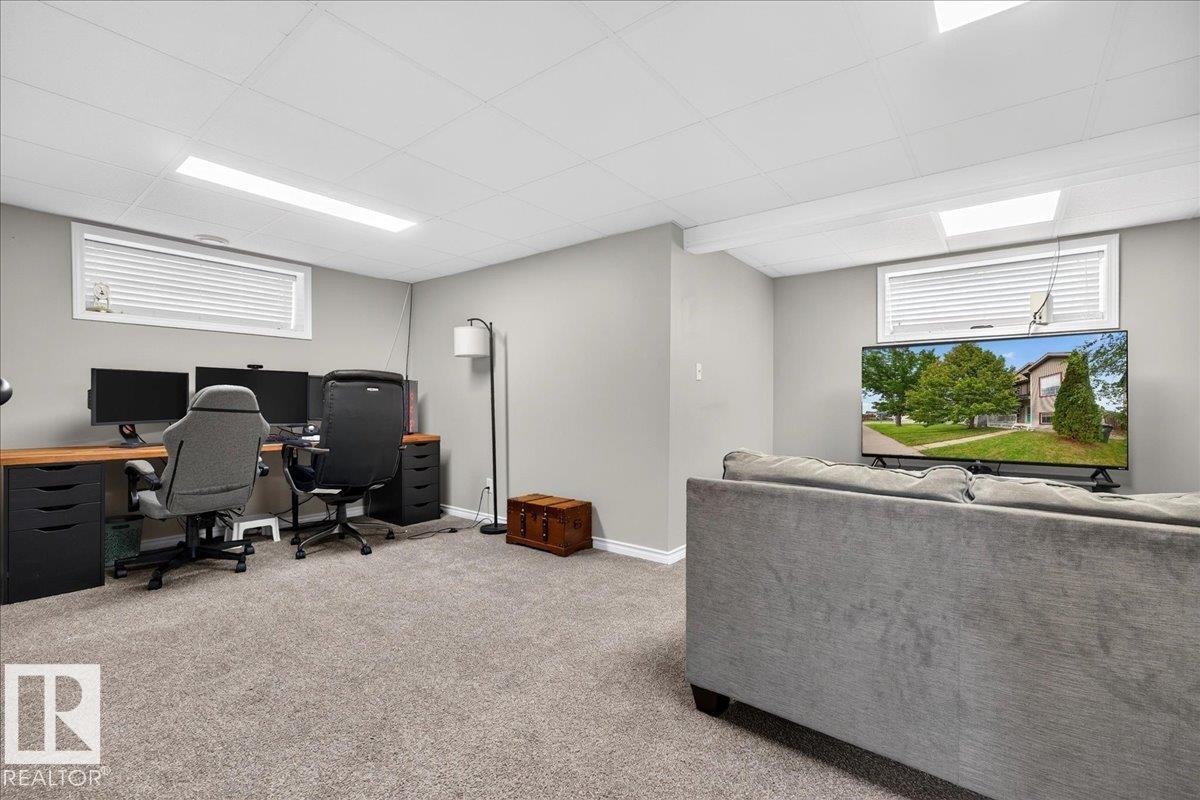 Finished Basement Recreation Area featuring carpeted flooring, recessed and linear ceiling lighting, large windows with cellular blinds, built-in desk workspace with storage cabinetry, and a comfortable seating zone with upholstered sectional sofa - 887 Oakland Boulevard, Devon, AB - Indoor Photo Showing Basement