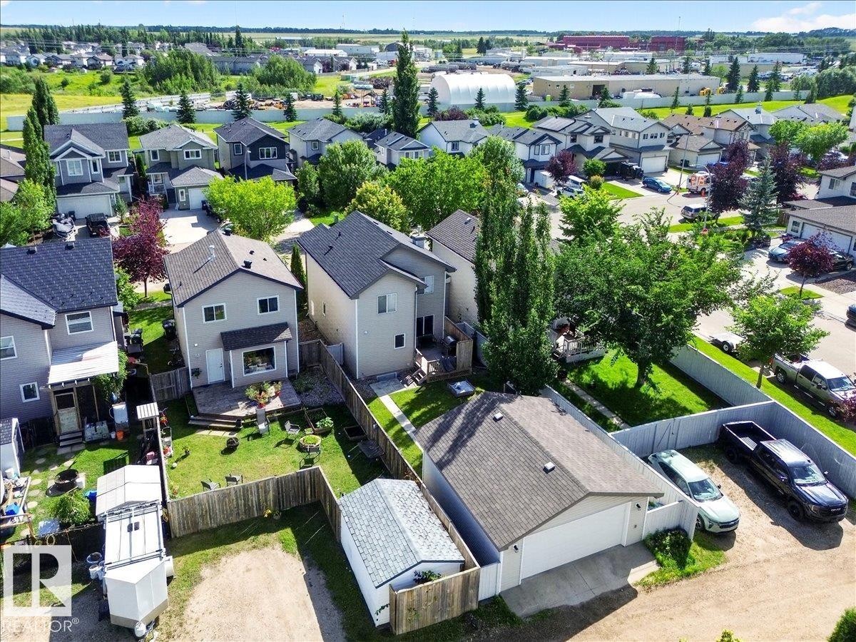 Aerial view showcasing a contemporary home with a dark-finished roof, expansive manicured lawn, mature landscaping with established trees, and detached garage - 887 Oakland Boulevard, Devon, AB - Outdoor