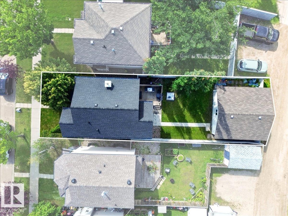 Property featuring a dark shingle roof, a paved walkway, a manicured lawn, and mature trees - 887 Oakland Boulevard, Devon, AB -