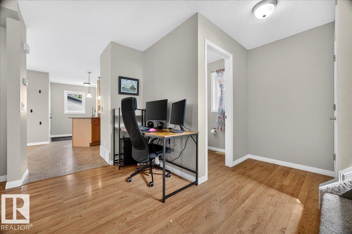 Versatile home office featuring wood-finish flooring throughout, dedicated workspace with dual-monitor setup, abundant natural lighting from recessed ceiling fixtures, and direct access to adjoining rooms - 887 Oakland Boulevard, Devon, AB - Indoor Photo Showing Office