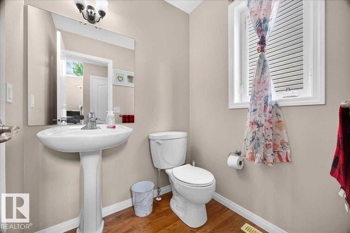 Pedestal sink with chrome faucet, large mirror, and wood-finish flooring - 887 Oakland Boulevard, Devon, AB - Indoor Photo Showing Bathroom