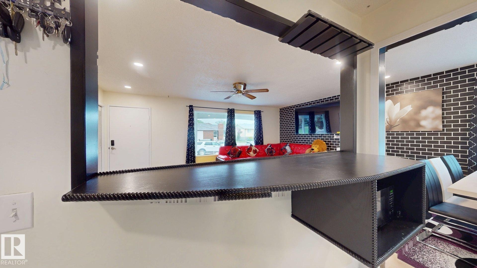 Pass-through window with an integrated countertop bar featuring textured trim and built-in shelving - 12812 45 Street Nw, Edmonton, AB - Indoor Photo Showing Other Room