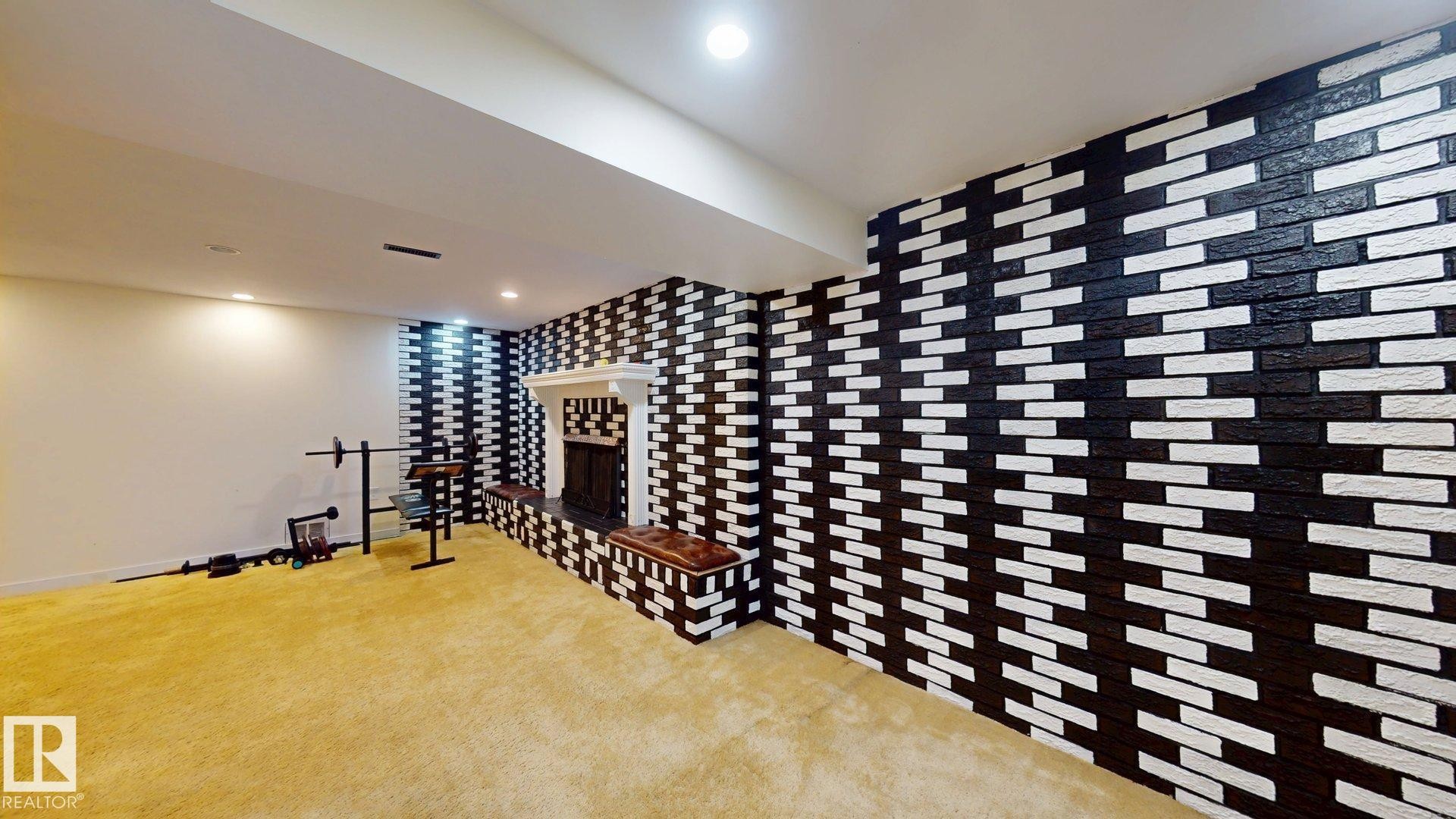 Spacious room featuring a fireplace with a detailed white mantel, black and white brick-patterned accent walls, recessed lighting, and soft gold carpeting - 12812 45 Street Nw, Edmonton, AB - Indoor Photo Showing Other Room