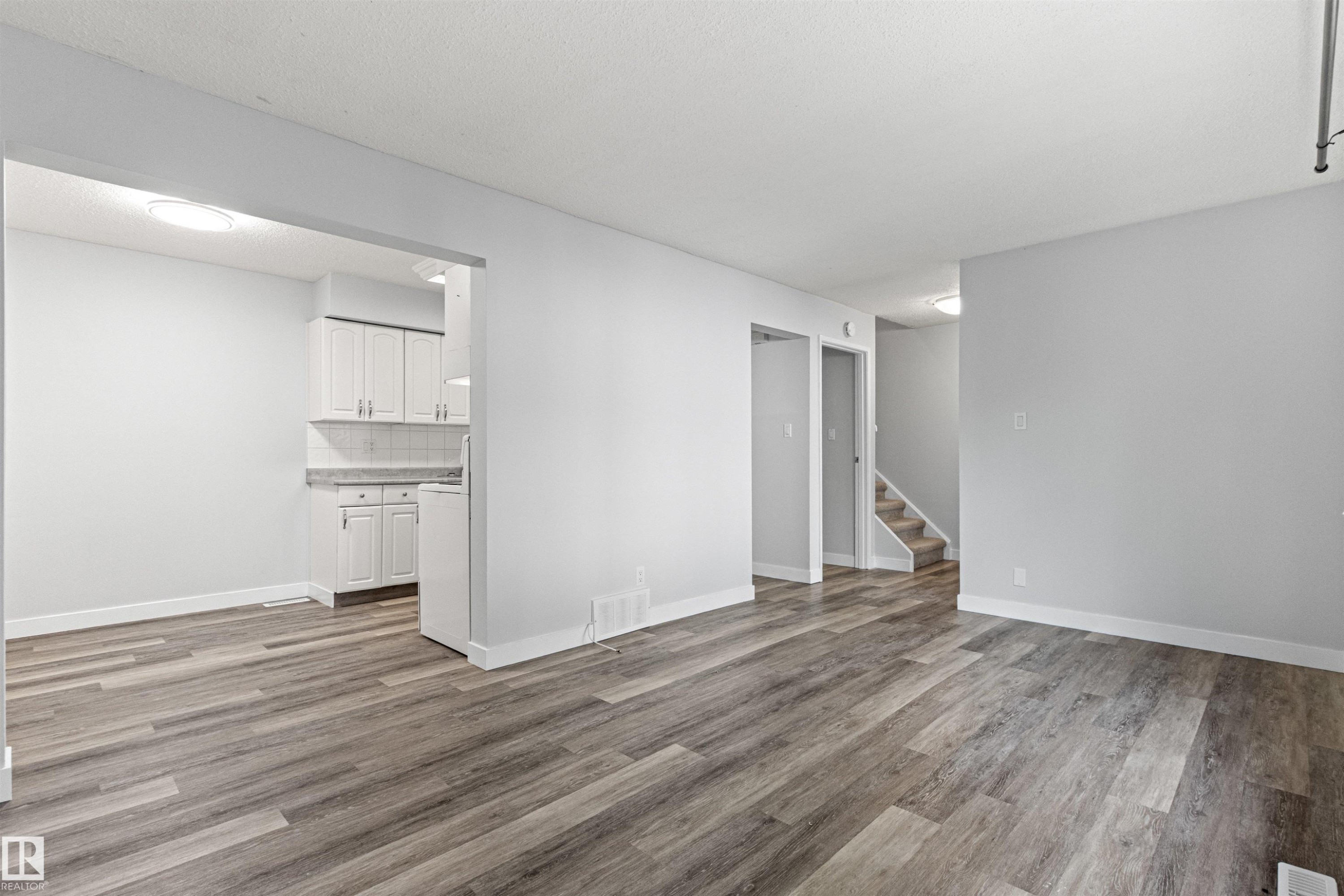 Wood-finish flooring throughout, white painted walls, white cabinetry with white subway tile backsplash, and a carpeted stairway - #9 14230 80 St Nw, Edmonton, AB - Indoor