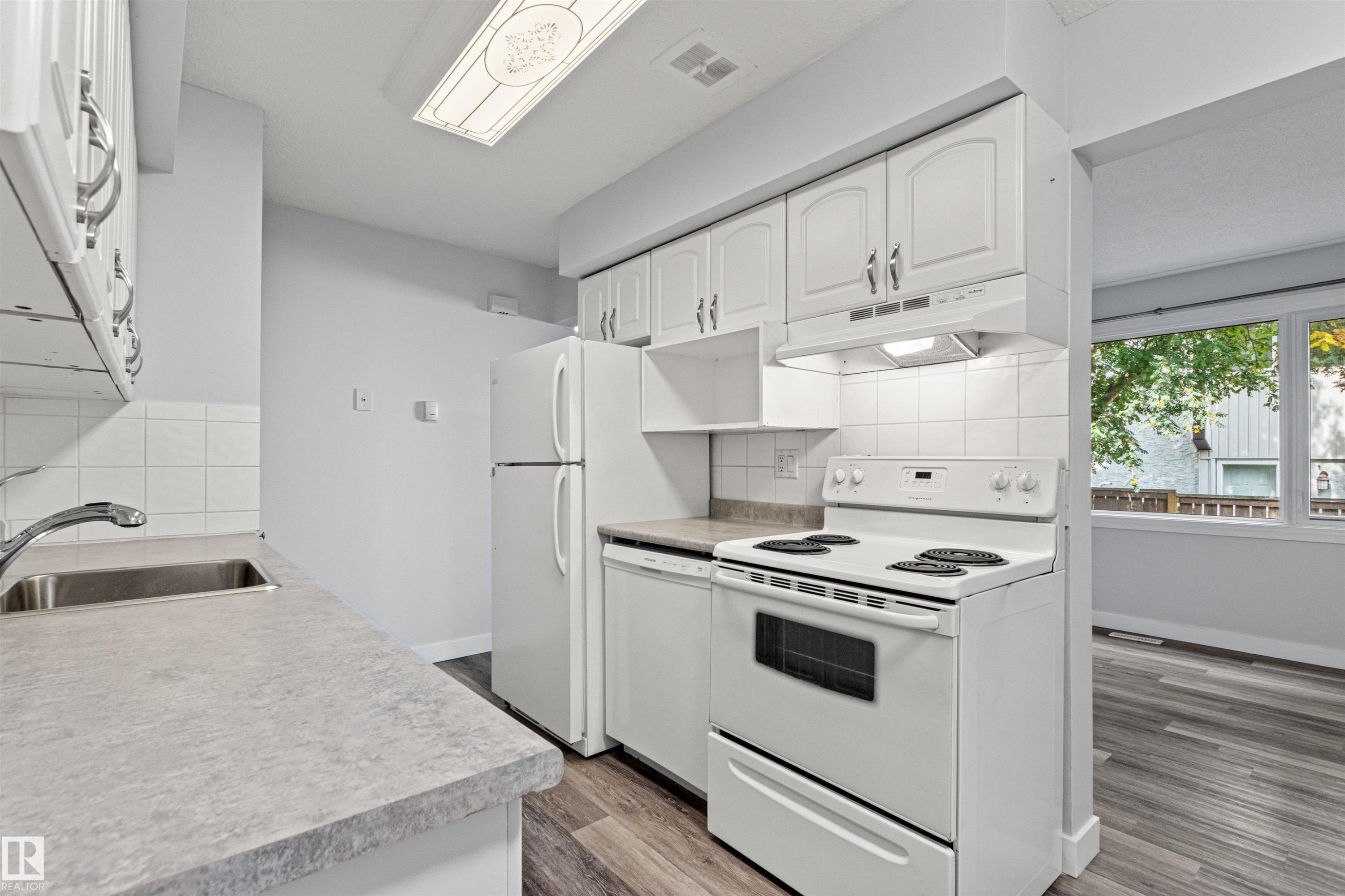 Kitchen featuring white cabinetry, a stainless steel sink, light-toned countertops, white appliances, and wood-finish flooring - #9 14230 80 St Nw, Edmonton, AB - Indoor Photo Showing Kitchen