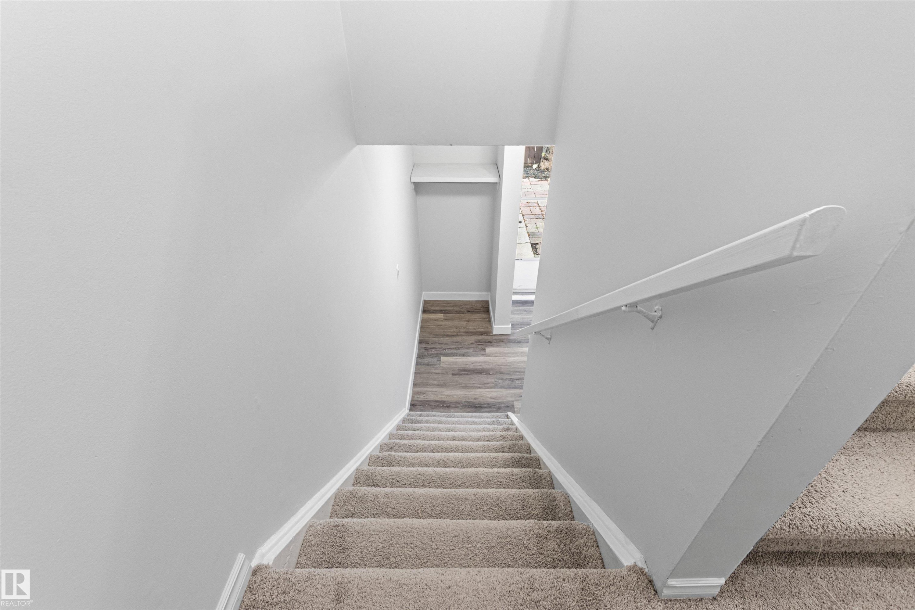 Carpeted staircase with wood-finish treads and white painted walls featuring a coordinating handrail - #9 14230 80 St Nw, Edmonton, AB - Indoor Photo Showing Other Room