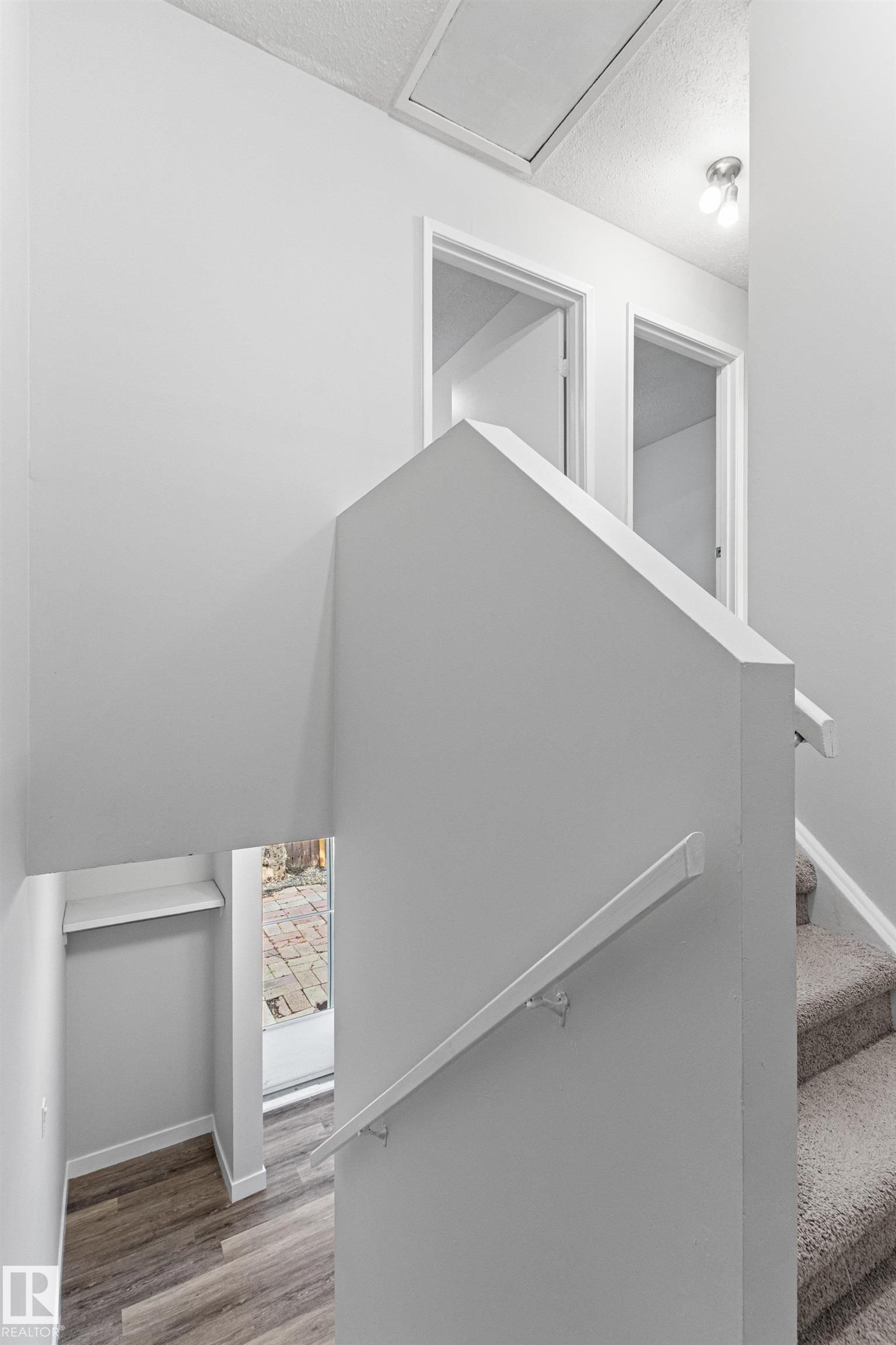 Carpeted staircase with wall-mounted handrail, leading to an upper landing with two doorways and overhead lighting - #9 14230 80 St Nw, Edmonton, AB - Indoor Photo Showing Other Room