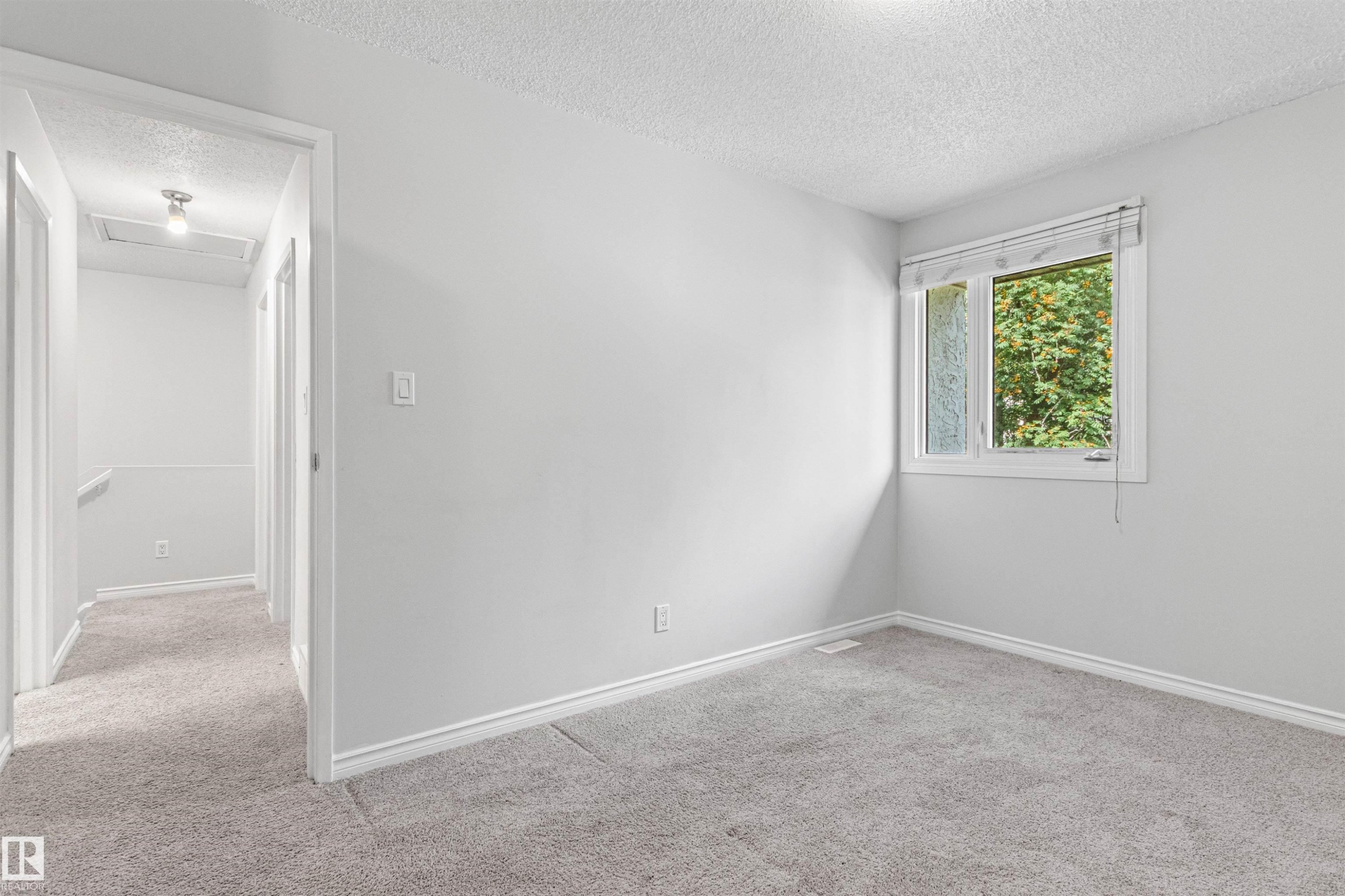 Bright secondary bedroom with neutral wall finishes, plush carpeting, and natural light from a casement window framed by lush exterior greenery - #9 14230 80 St Nw, Edmonton, AB - Indoor Photo Showing Other Room