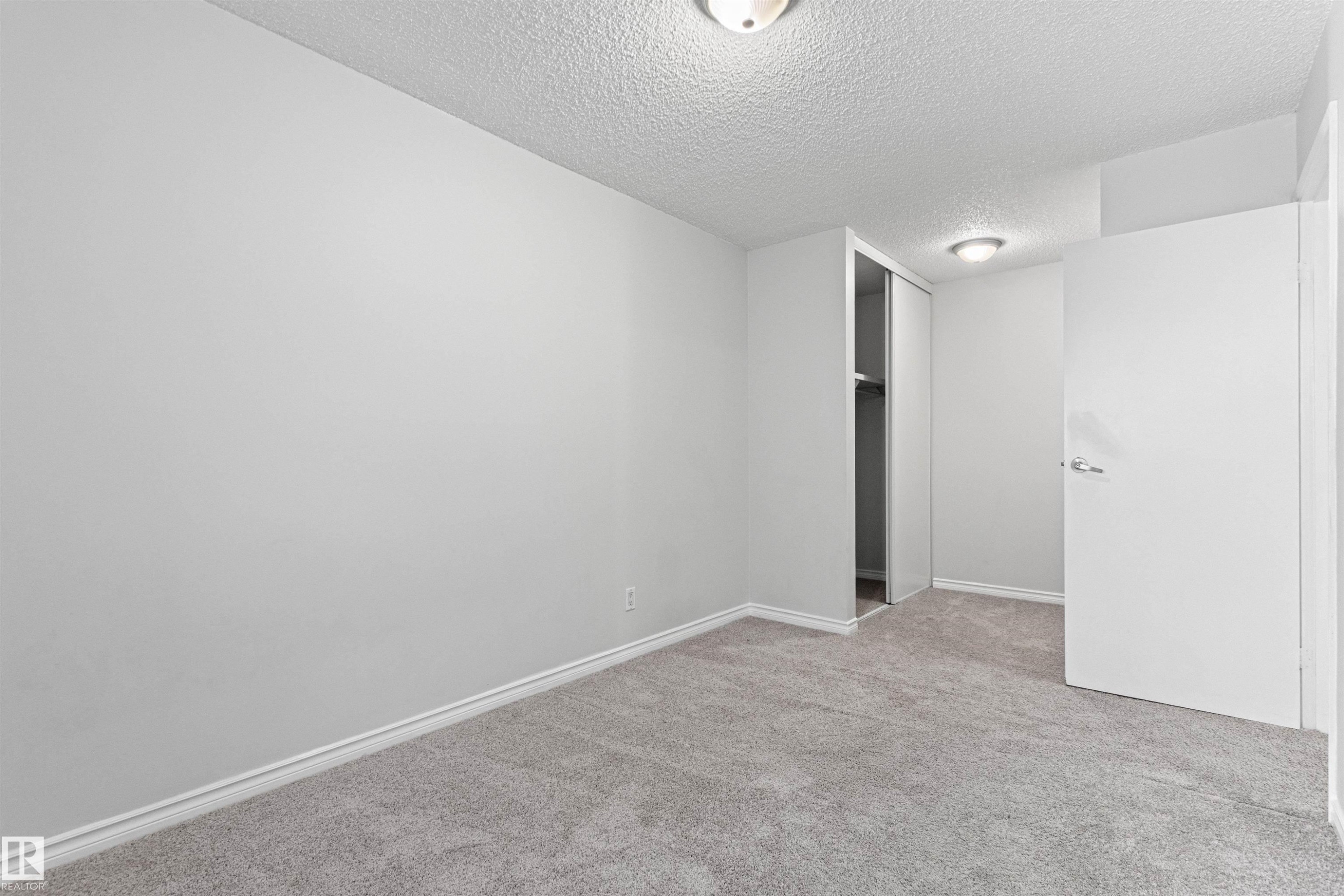 Neutral gray carpeting, white painted walls, white baseboards, and a built-in closet with sliding doors - #9 14230 80 St Nw, Edmonton, AB - Indoor Photo Showing Other Room